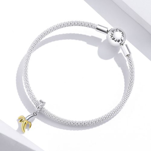 Finom ezüst hálós karkötőre fűzött lógós banán charm, a háttérben a karkötő elegáns, gömb alakú, Love forever feliratú kapcsával.