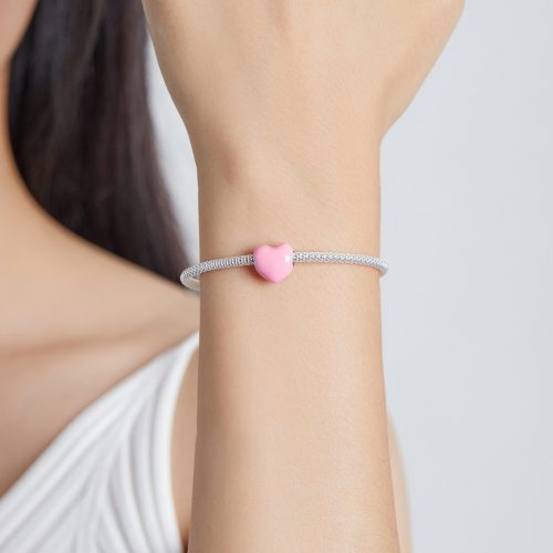 Női csuklón viselt, finom hálós ezüst karkötő egyetlen elegáns, minimalista rózsaszín szív charm kiegészítővel díszítve.