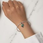 Elegant módon viselt ezüst hálós karkötő és a rajta függő csillogó kék-zöld kaméleon charm egy női kézen bemutatva, fehér ingujjal és márvány felülettel.