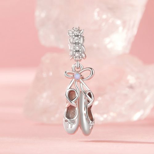 Csillogó kövekkel díszített ezüst balerina cipő függő ékszer charm elegáns, púderrózsaszín stúdióháttérben bemutatva.